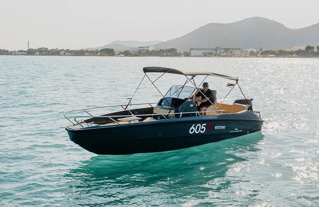 OceanMaster 605 with the bimini top up, on sparkling water in front of the coast